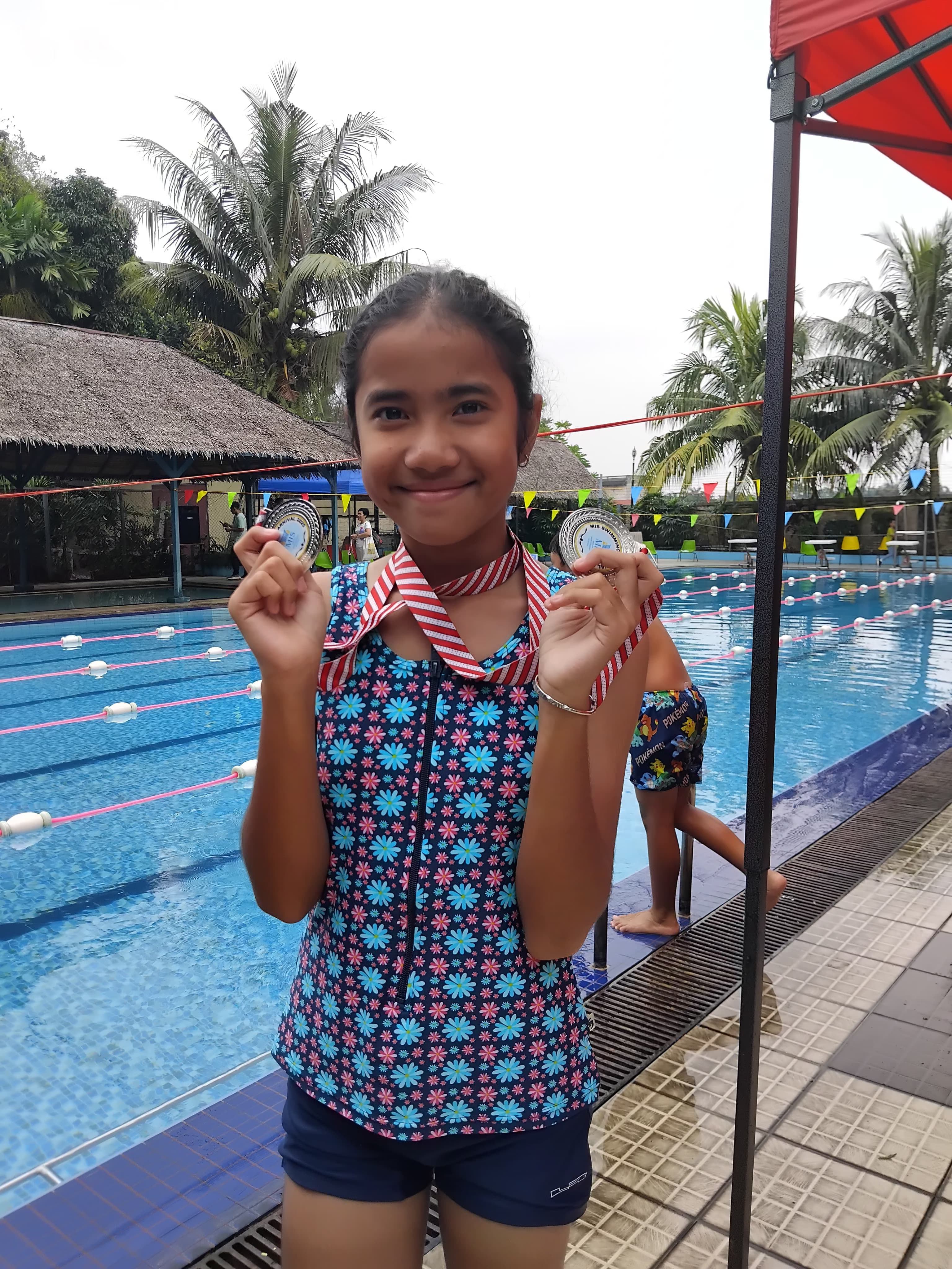 Perenang muda tersenyum memegang medali di arena lomba